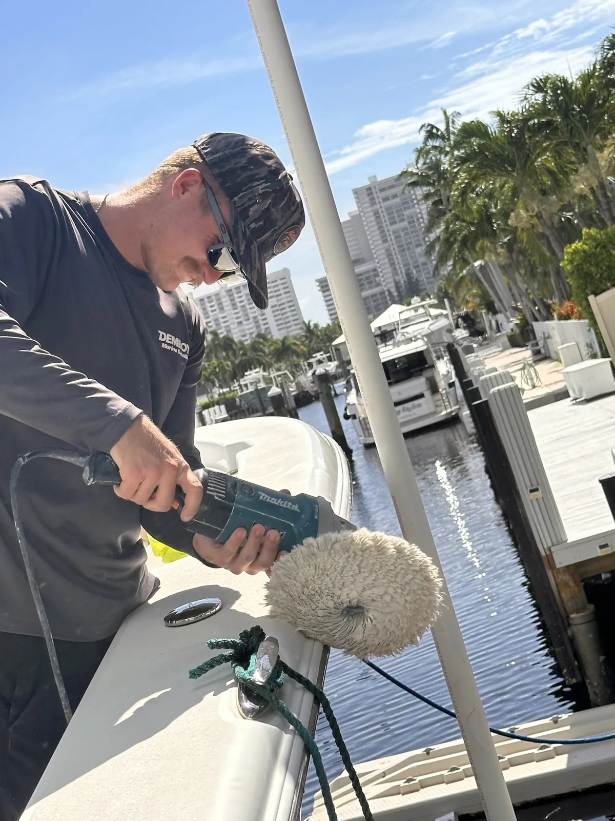 Detailer holding a Makita buffer with a wool pad while polishing a boat at a marina dock in Delray Beach, FL