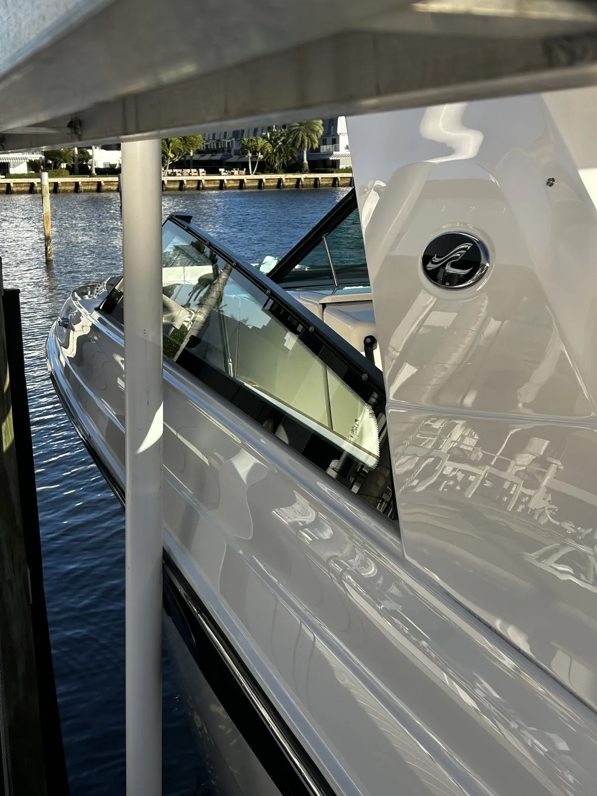 Glossy white boat on a lift under a canopy beside a canal in Tropic Isles, Delray Beach, Florida after a boat detail