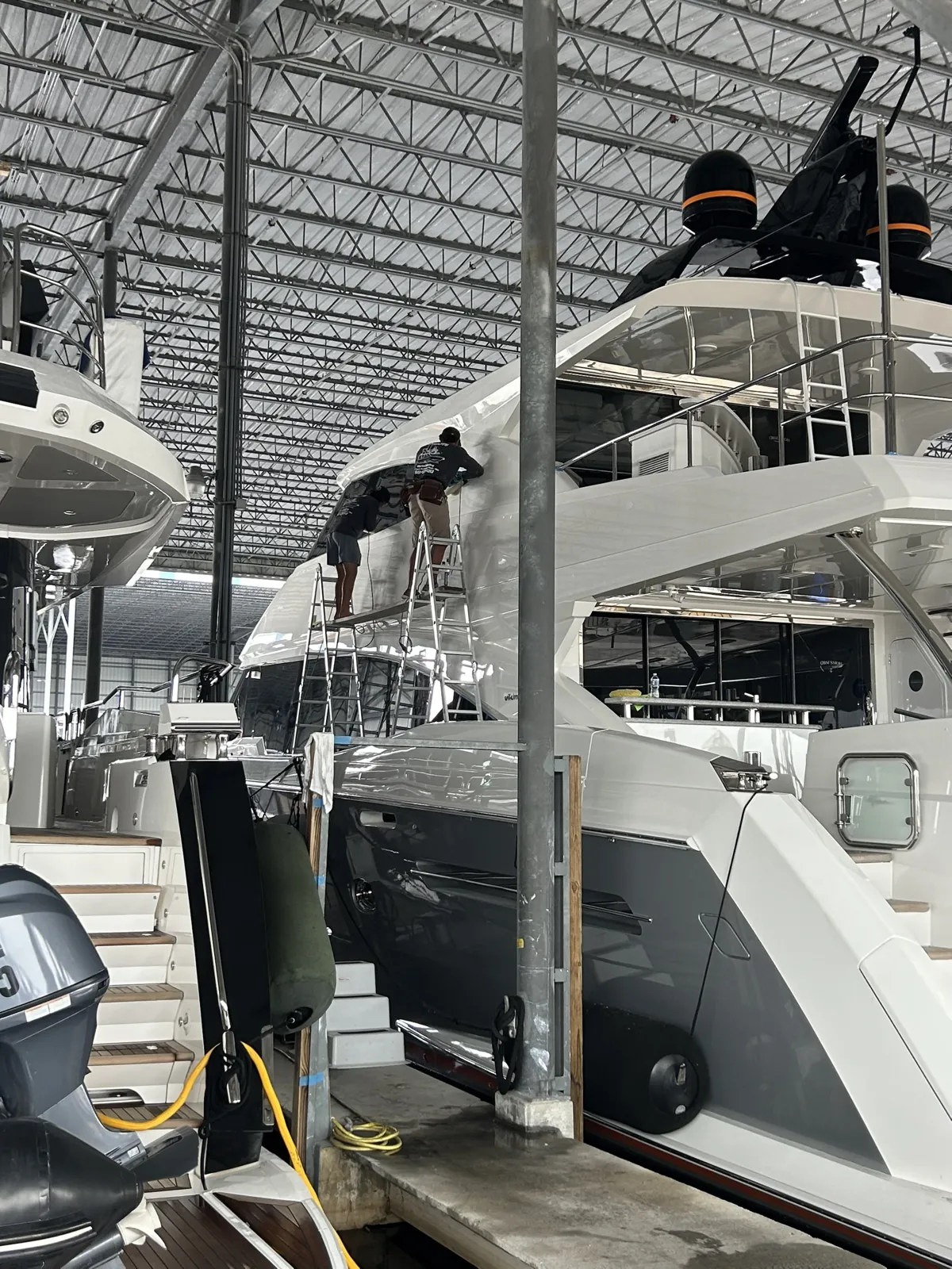 Detailers on ladders polishing the side of a yacht in a covered boat shed at Bradford Marine, Fort Lauderdale