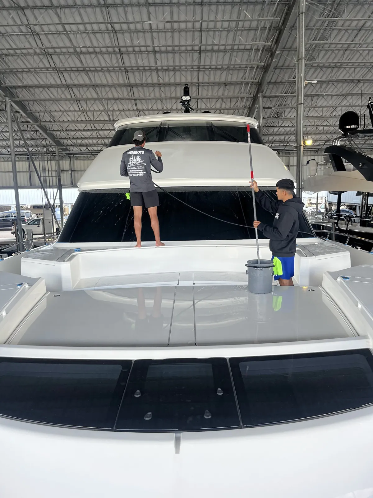 Two detailers washing the windshield and cabin top of a large yacht in a covered shed at Bradford Marine, Fort Lauderdale
