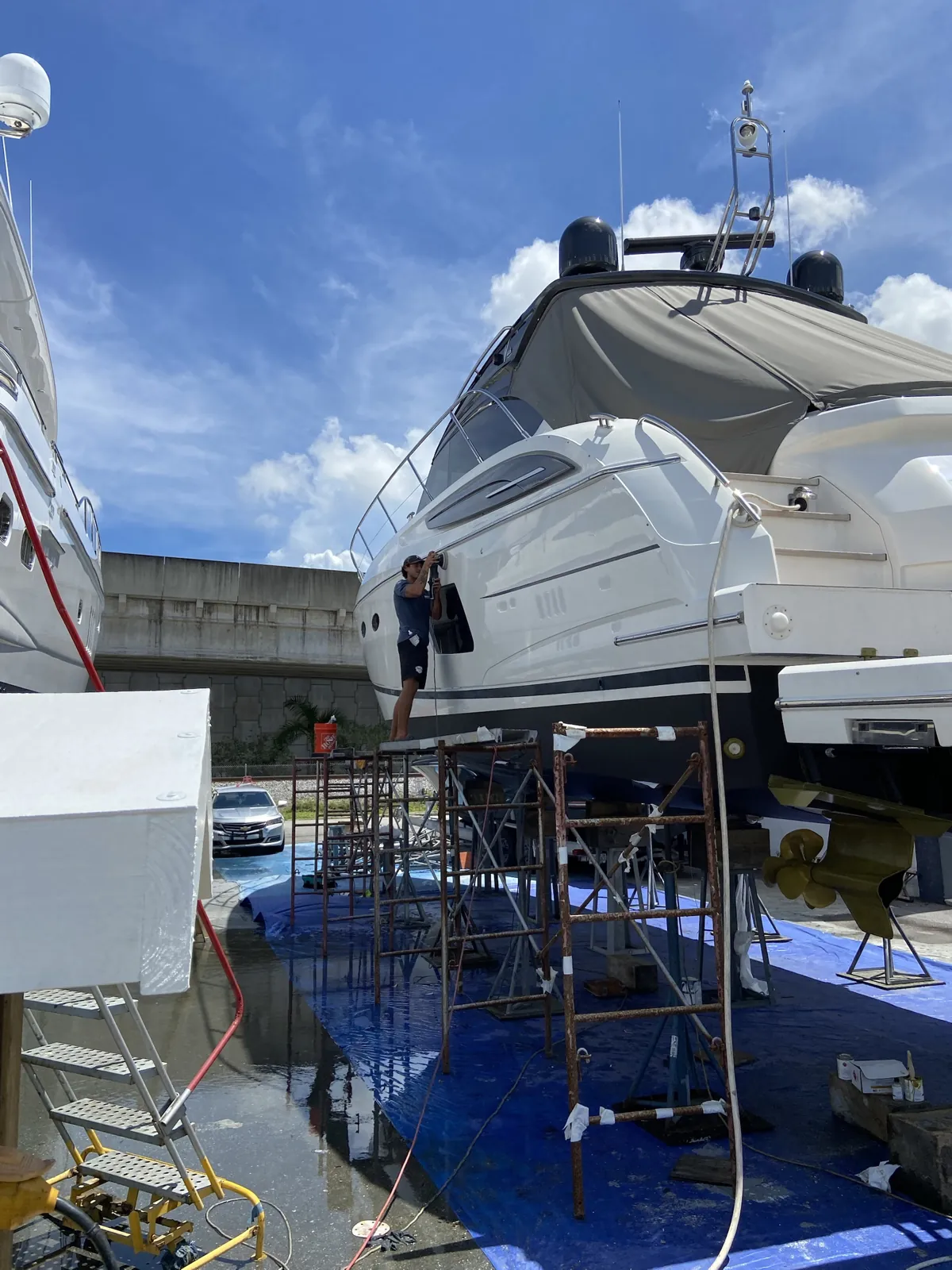 Detailer on a scaffold machine-polishing the side of a white yacht on blocks in a Fort Lauderdale boat yard