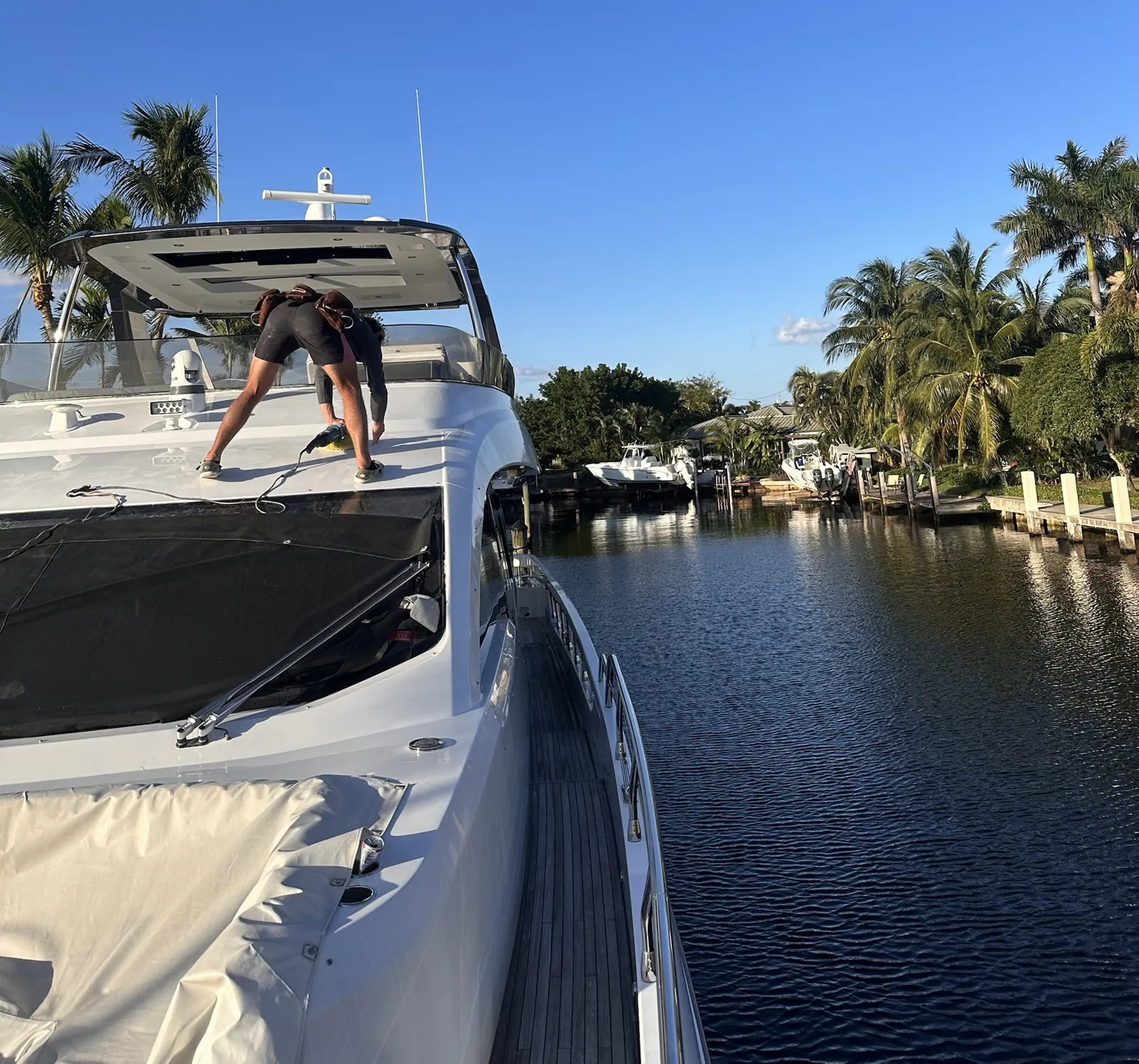 Detailer polishing a yacht foredeck beside a palm-lined canal at The Landings in Fort Lauderdale, FL