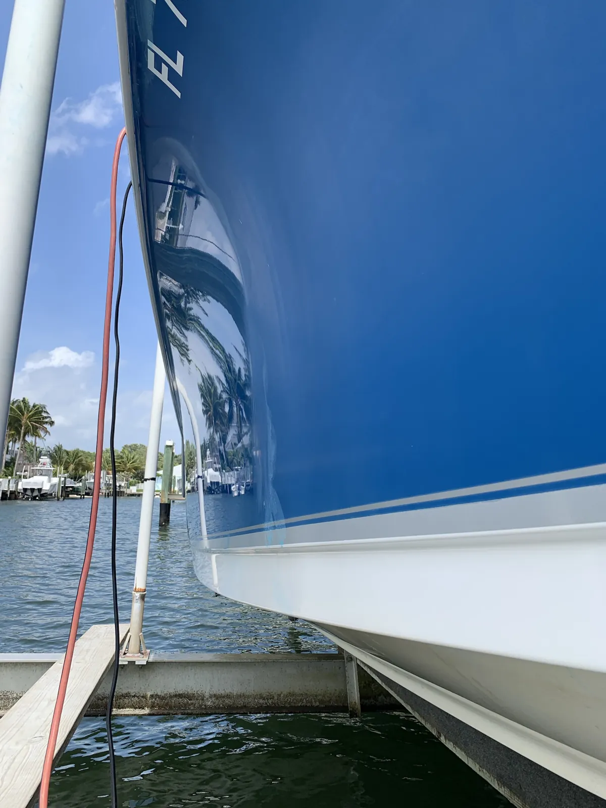 Deep blue boat hull on a boat lift in Jupiter, FL polished to a mirror finish that reflects palm trees