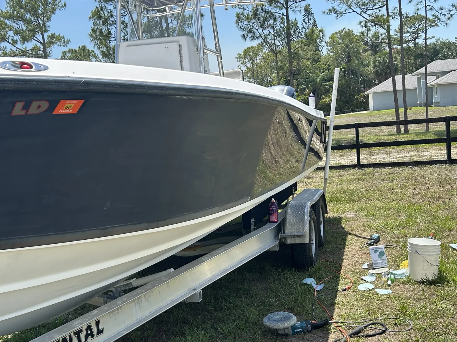Boat hull on a trailer in Loxahatchee, Florida partway through sanding and polishing, with sanding discs and a sander on the grass