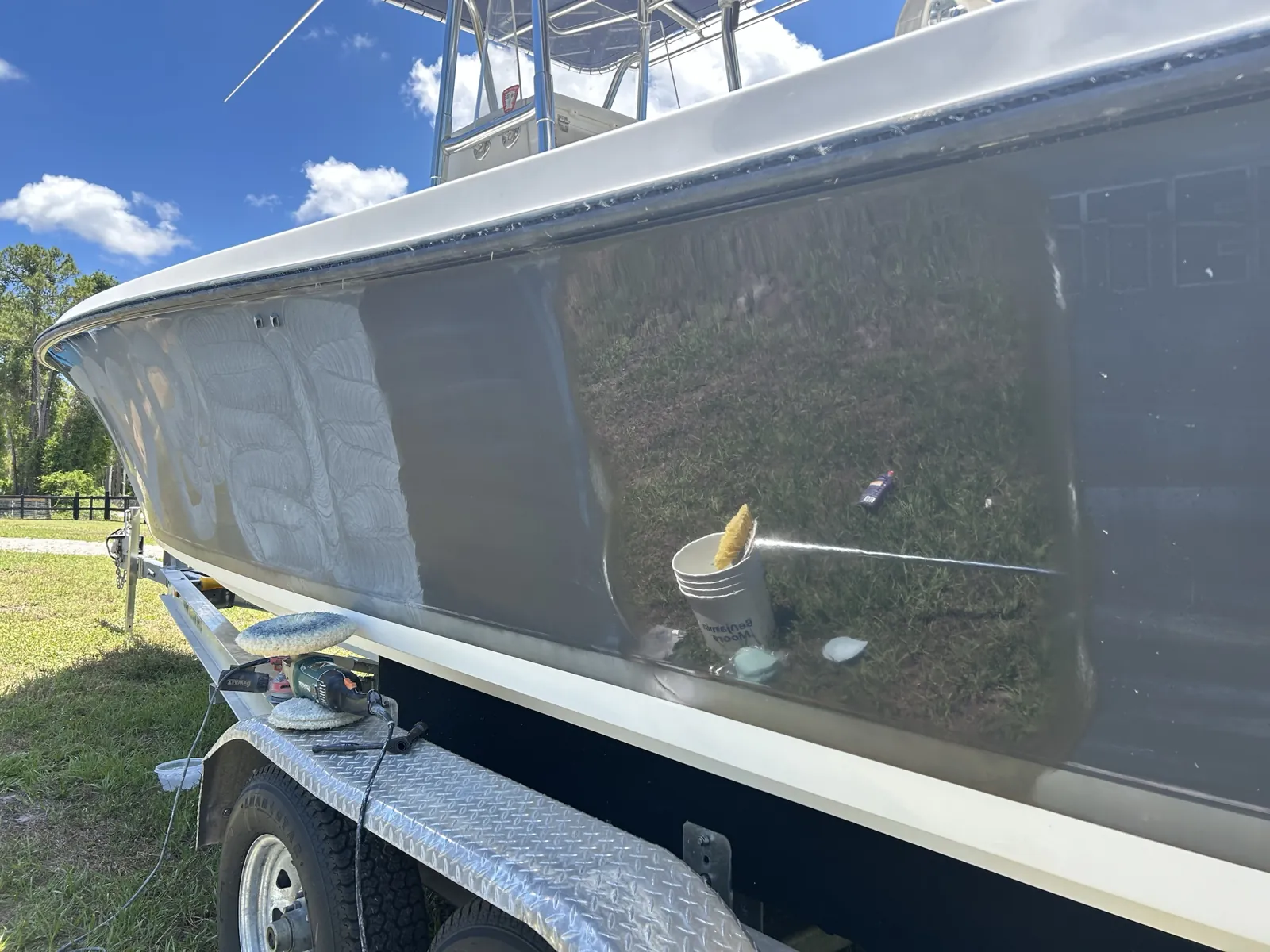 Gray boat hull on a trailer in Loxahatchee, FL midway through compounding, with swirl marks beside a mirror-finish section