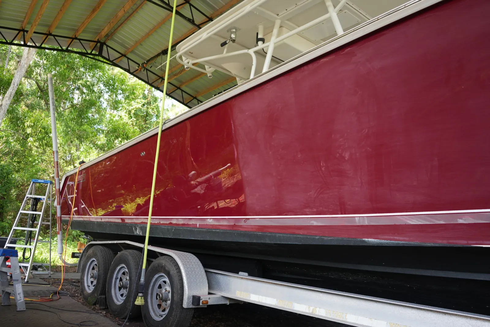 Red boat hull on a trailer in Loxahatchee, Florida with one half compounded to a deep gloss and the other half still dull