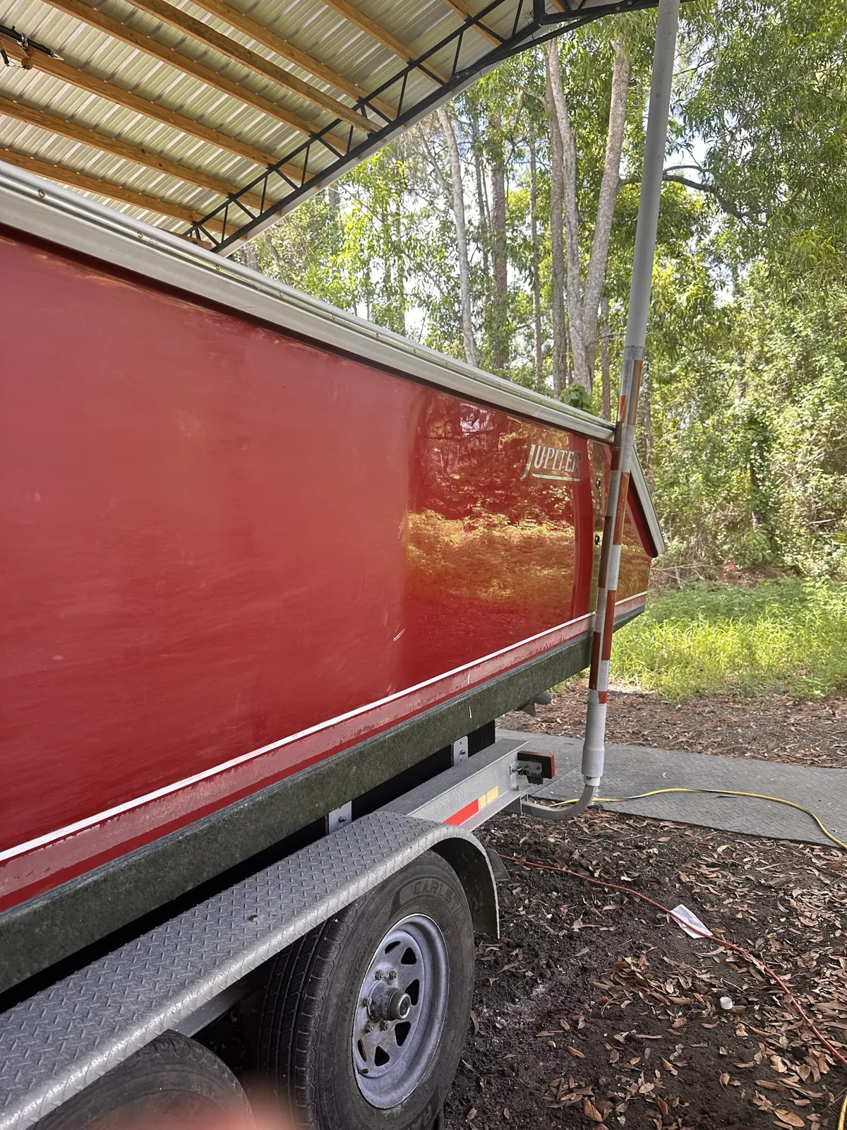 Red Jupiter-brand center console on a trailer under a metal roof in Loxahatchee, FL, polished to a deep gloss