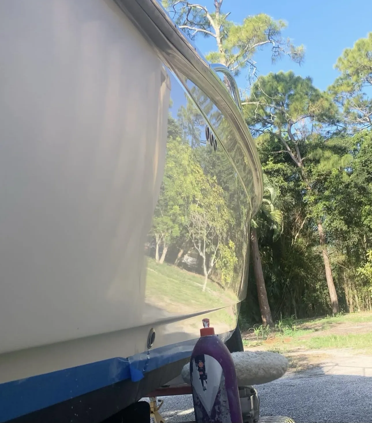 Scout boat hull on a trailer in Loxahatchee, FL reflecting pine trees, with the compounded side glossy next to the dull side